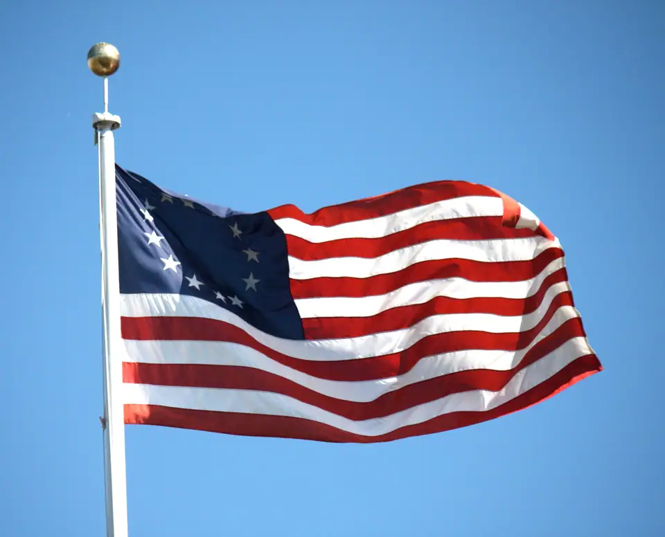 A Betsy Ross flag with thirteen stars in a circle flying from a pole against a clear blue sky