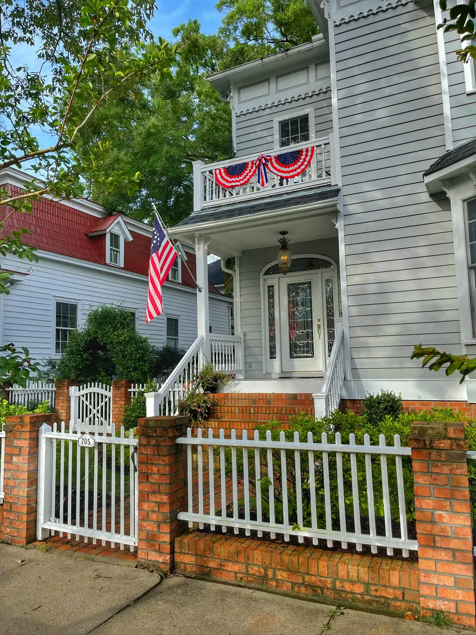 A white wooden house with red, white and blue bunting on the porch and a picket fence