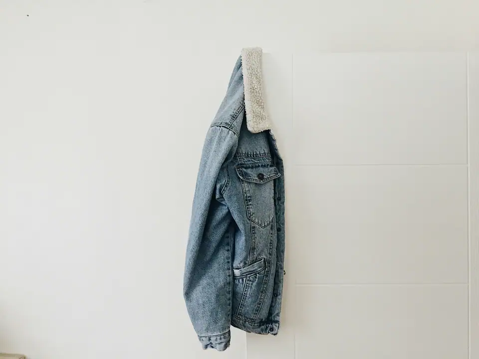 A light-wash denim jacket hanging on a white door