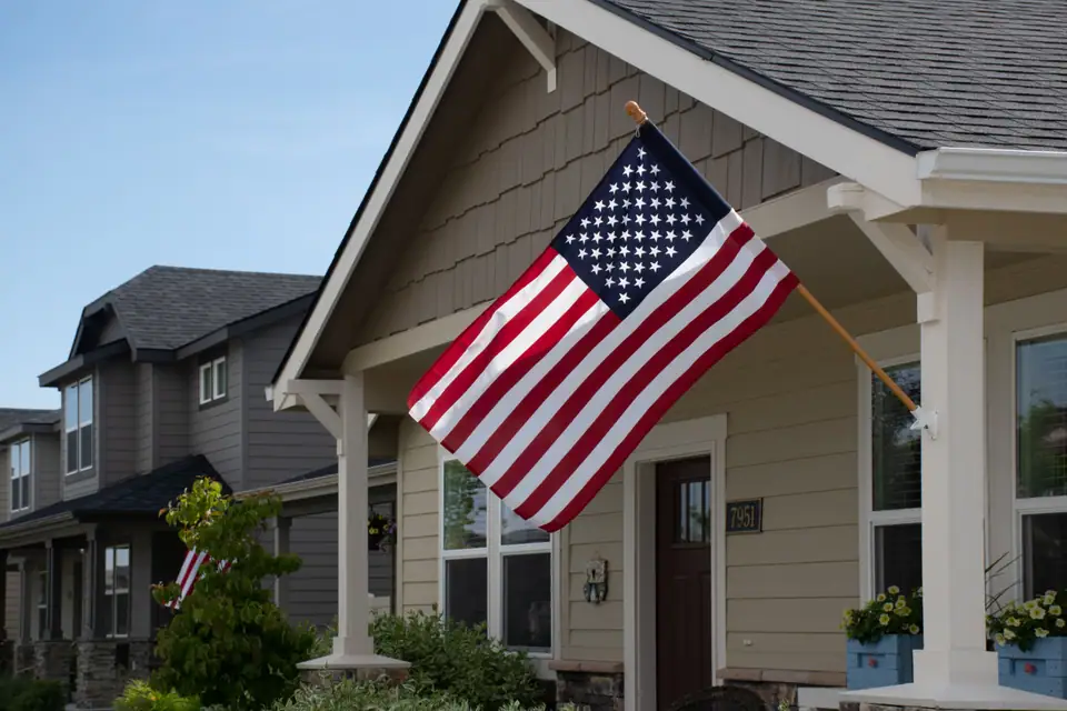 An American flag flying from a bracket outside a gray suburban house