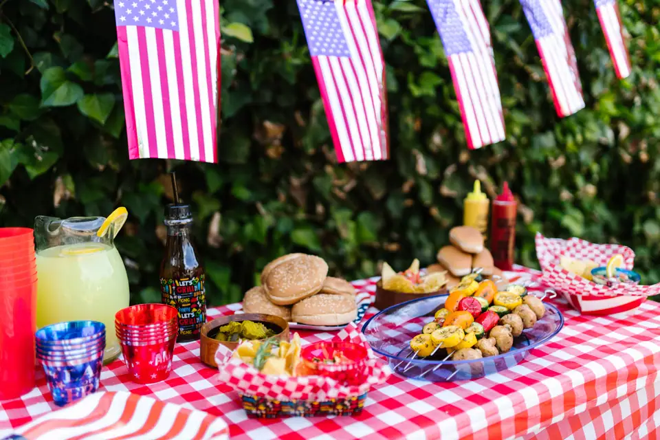 A Fourth of July picnic table with small American flags, lemonade and burgers on a checked cloth