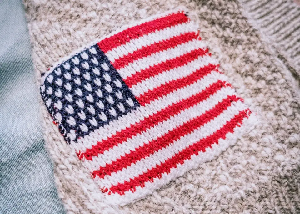 Close-up of a knitted American flag patch on a gray sweater