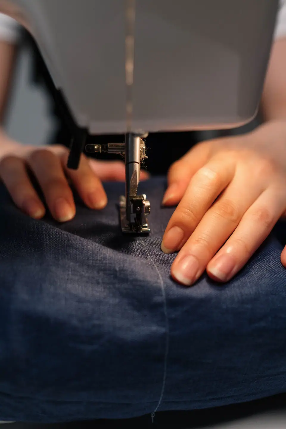 Hands guiding navy fabric under the foot of a sewing machine